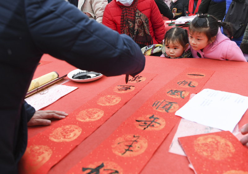 Des enfants regardent un calligraphe écrire des couplets de la fête du Printemps pour les habitants lors d'une activité de composition de couplets dans l'arrondissement de Yongchuan