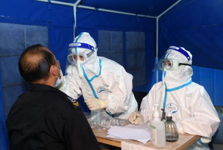 (miniature) Des professionnels de santé effectuent un prélèvement de gorge sur un habitant dans un site de test d'acide nucléique