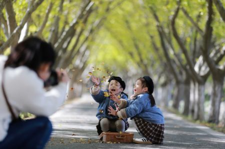(miniature) Une femme prend des photos d'enfants jouant avec des feuilles mortes dans un parc de l'arrondissement de Jiangdu à Yangzhou
