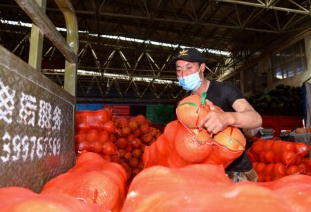 (miniature) Un membre du personnel porte un sac de citrouilles au centre de commerce de légumes du marché de gros des produits agricoles de Xinjiang Jiuding à Urumqi