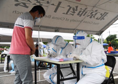 (miniature) Des membres du personnel enregistrent les informations d'un habitant (1er à gauche) afin d'effectuer un test d'acide nucléique dans un site de prélèvement de l'arrondissement de Fengtai