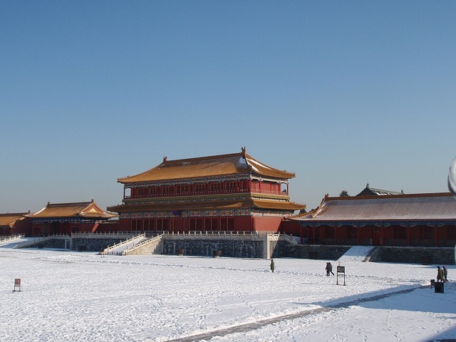 Le belvédère de la Bienveillance incarnée sous un ciel bleu d’hiver, ses deux toits couverts de neige, avec des visiteurs dans la cour enneigée au premier plan.