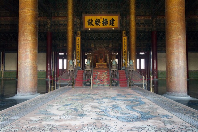 L’intérieur de la salle de l’Harmonie suprême : un tapis à dragons bleus mène, entre des colonnes dorées, au trône posé sur une estrade rouge sous une plaque calligraphiée.