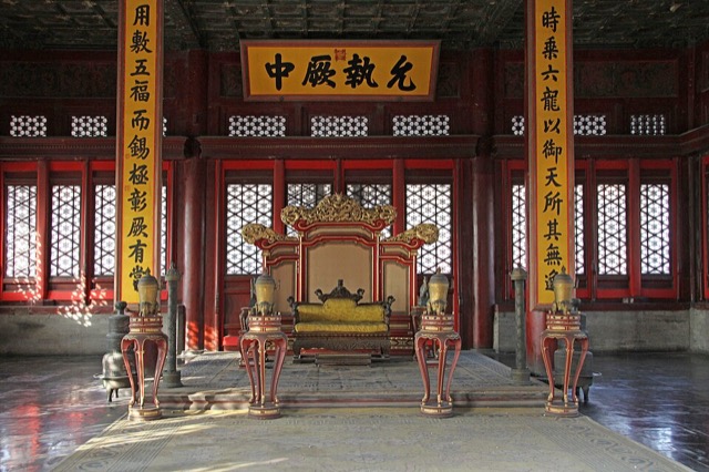 L’intérieur de la salle de l’Harmonie parfaite : un trône doré sur une petite estrade, entre deux colonnes rouges portant des sentences verticales, sous une plaque calligraphiée.