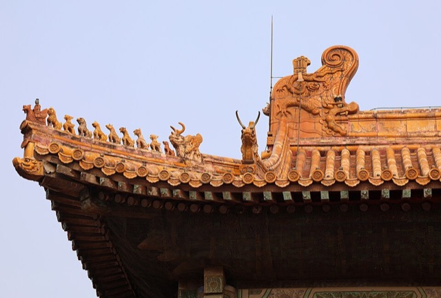 Gros plan sur un angle du toit de la salle de l’Harmonie préservée : une file de neuf figurines dorées derrière un personnage chevauchant un oiseau, et une grande queue de dragon vernissée au sommet.