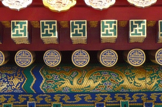 Gros plan sur le dessous de l’avant-toit : bouts de chevrons peints d’un motif vert et or, chevrons ronds ornés du caractère de la longévité, et frise de dragons dorés.