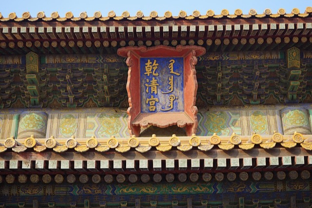 Gros plan sur la plaque bleue à cadre rouge du palais de la Pureté céleste, entre deux rangées de tuiles vernissées jaunes et des poutres peintes.
