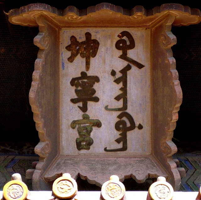 Gros plan sur la plaque du palais de la Tranquillité terrestre : trois caractères chinois à gauche, l’écriture mandchoue à droite, dans un cadre sculpté.