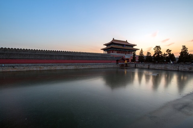 La porte de la Prouesse divine et le mur d’enceinte crénelé se reflètent dans la douve gelée, au crépuscule d’un jour d’hiver.