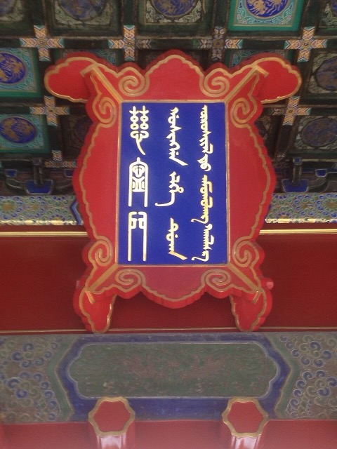Plaque bleue à cadre rouge et or, écrite en chinois et en mandchou, suspendue sous un plafond à caissons peints.