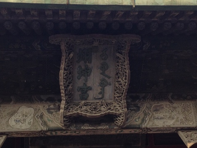 La plaque du palais de l’Honneur terrestre sous l’avant-toit : trois caractères chinois et l’écriture mandchoue sur fond sombre, dans un cadre de bois ajouré sculpté de dragons.