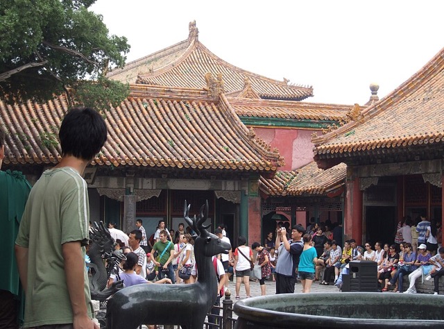 Un cerf et un dragon de bronze devant les toits jaunes du palais de l’Élégance rassemblée, avec la foule des visiteurs dans la cour.