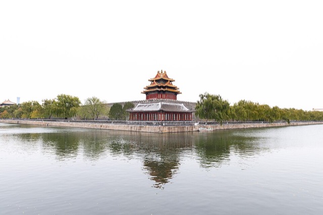 Tour d’angle et son pavillon reflétés dans l’eau immobile de la douve, sous un ciel blanc d’hiver.