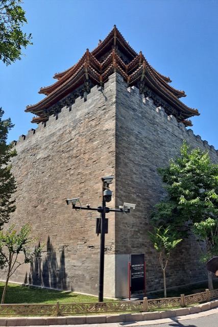 Angle du mur de briques grises vu d’en bas, surmonté des avant-toits superposés d’une tour d’angle.