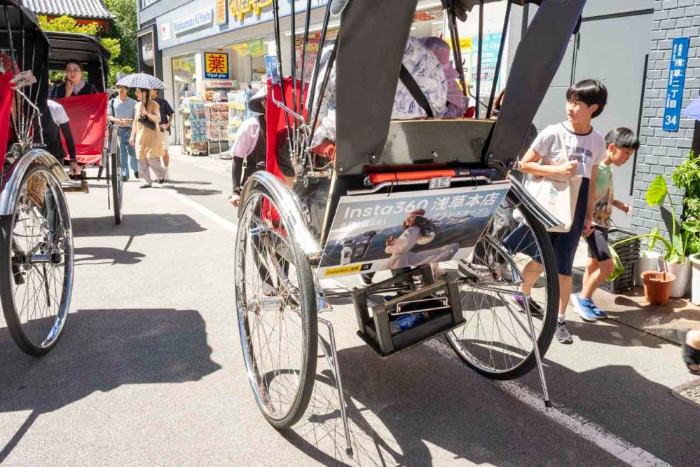 Un pousse-pousse touristique d'Asakusa porte une affiche annonçant l'ouverture du magasin Insta360, dans une rue commerçante