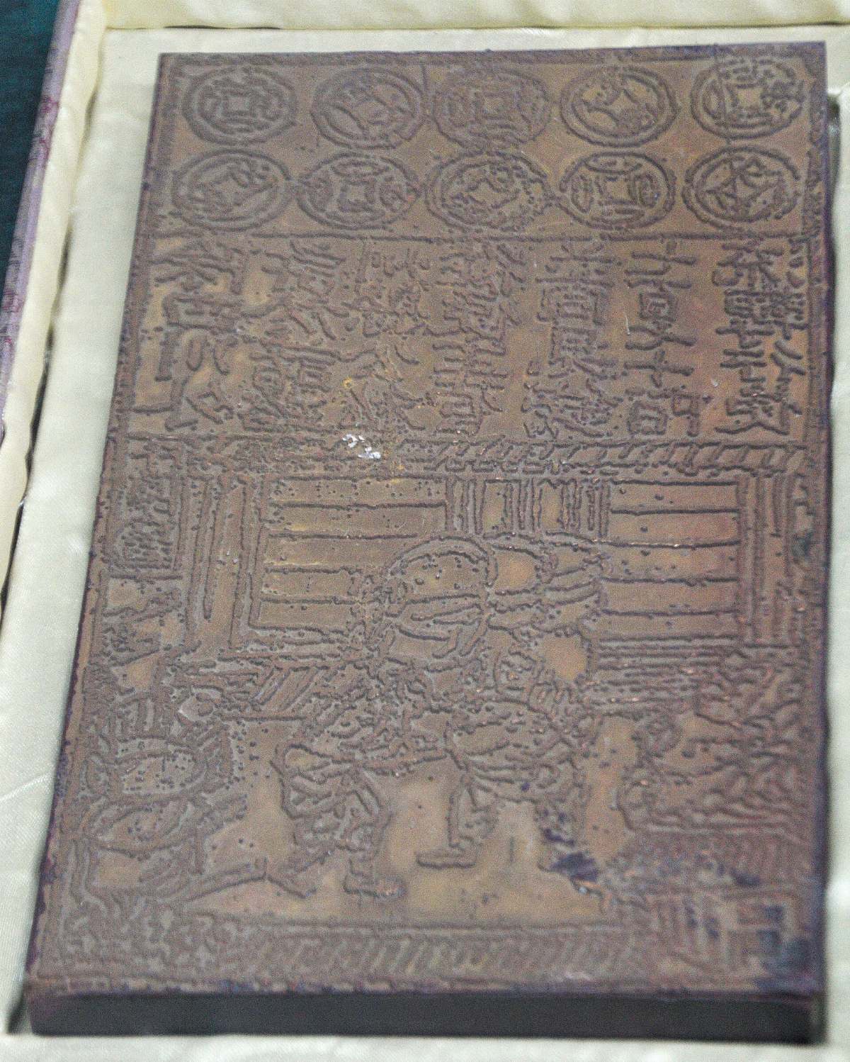 Plaque de cuivre gravée d'un billet des Song du Nord dans un écrin : motifs de pièces en haut, texte au milieu, porteurs et ballots en bas