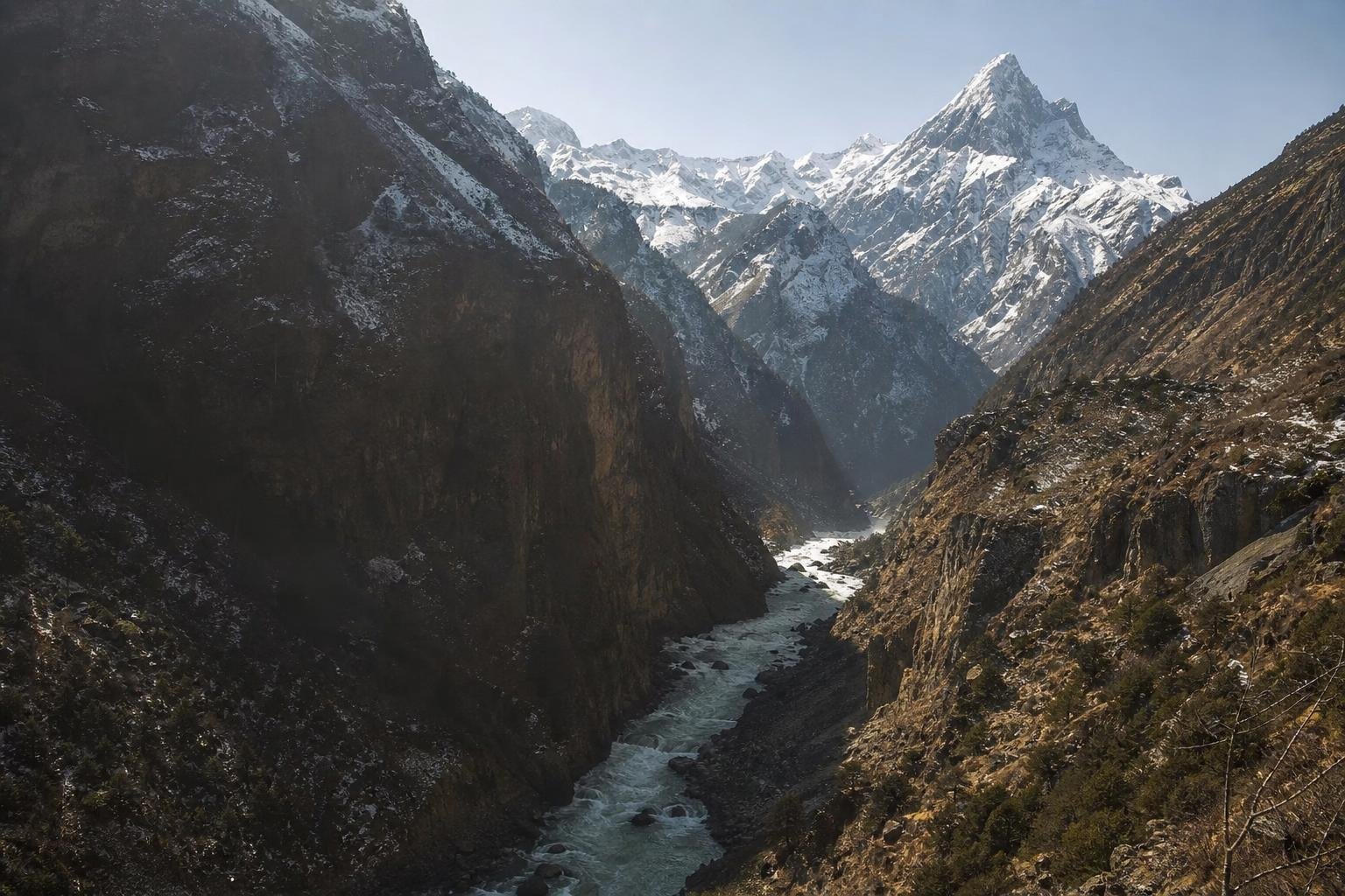 Gorge profonde parcourue par une rivière en crue entre des parois sombres, sommets enneigés au fond