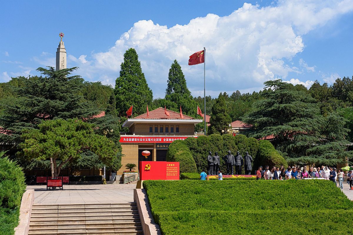 Le mémorial de Xibaipo : obélisque à étoile rouge, drapeau chinois, groupe de statues de bronze et visiteurs devant un bâtiment à toit de tuiles rouges