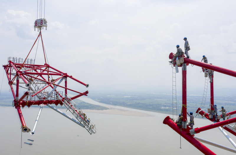 Photo aérienne prise le 16 août 2022 montrant des techniciens travaillant sur le site de construction de la tour nord de transmission d'électricité du projet de transmission d'électricité à courant continu ultra-haute tension (UHV) de 800 kilovolts de Baihetan-Zhejiang sur le fleuve Yangtsé à Tongling