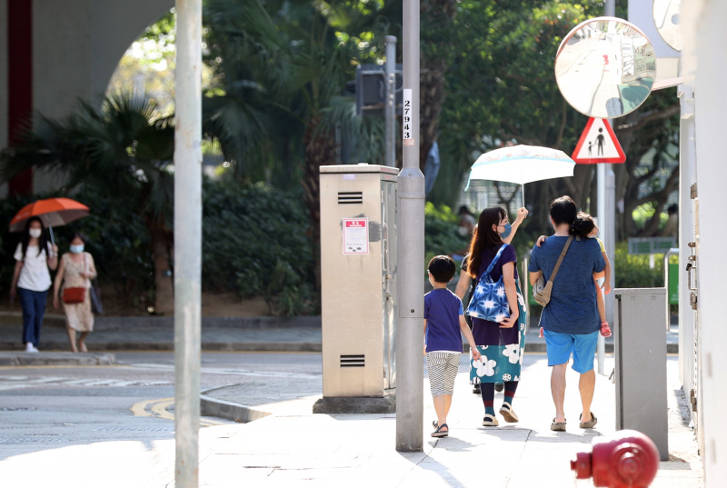 Des gens utilisent des ombrelles pour se protéger du soleil tout en marchant dans la rue lors d'une journée chaude d'été à Hong Kong