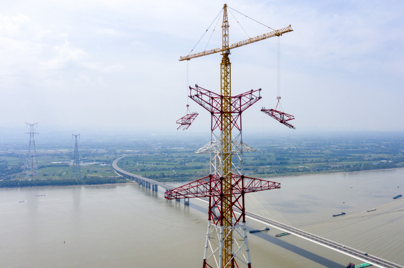 Photo aérienne prise le 16 août 2022 montrant des techniciens travaillant sur le site de construction de la tour nord de transmission d'électricité du projet de transmission d'électricité à courant continu ultra-haute tension (UHV) de 800 kilovolts de Baihetan-Zhejiang sur le fleuve Yangtsé à Tongling