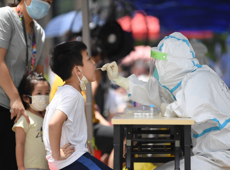 Un membre du personnel médical en combinaison de protection prélève un échantillon de gorge sur un adolescent pour des tests d'acide nucléique dans le quartier de Baihedong dans l'arrondissement de Liwan à Guangzhou