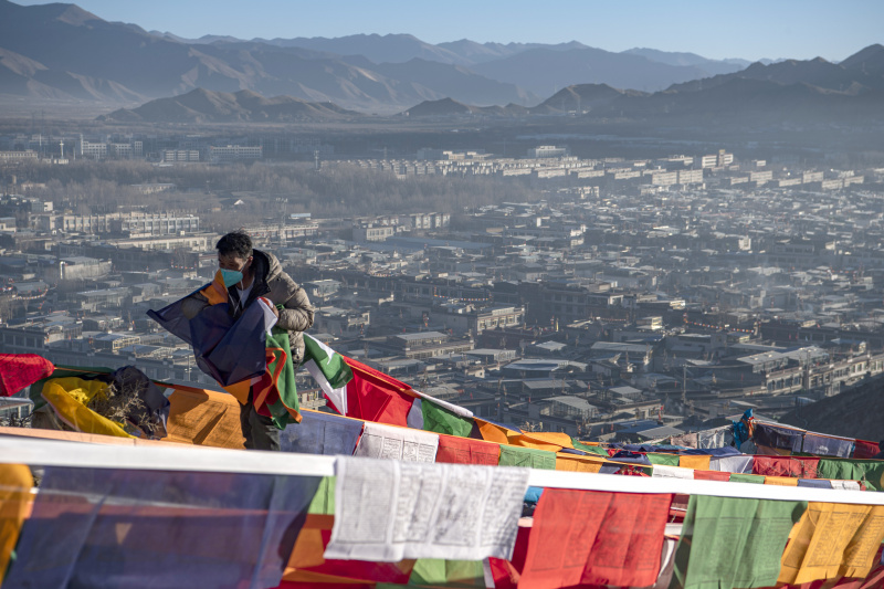 Un homme accroche des drapeaux de prières sur une montagne à Xigaze
