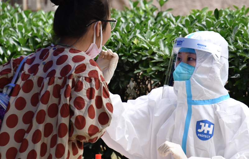 Un agent médical prélève un échantillon de gorge sur une habitante pour un test d'acide nucléique à Balizhuang dans l'arrondissement de Chaoyang