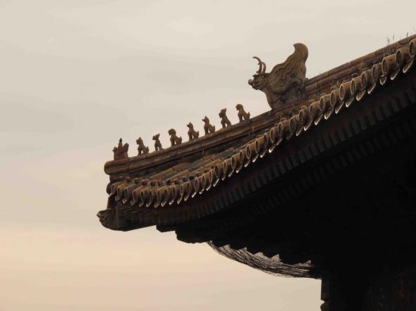 Angle de toiture en contre-plongée : une file de statuettes d’animaux court le long de l’arête jusqu’à une tête de dragon