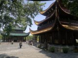 La tour de Yueyang vue de côté, trois niveaux de bois sombre aux avant-toits de tuiles jaunes retroussés, à côté d'un pavillon à toit vert, sur une esplanade dallée