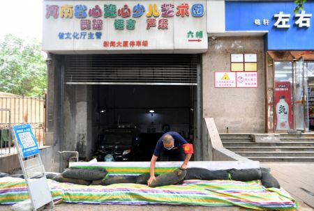(miniature) Un homme place des sacs de sable devant l'entrée d'un garage souterrain à Zhengzhou