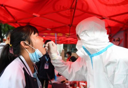 (miniature) Un membre du personnel médical prélève un échantillon de gorge sur une habitante pour un test d'acide nucléique dans un quartier du bourg de Shangpai du district de Feixi
