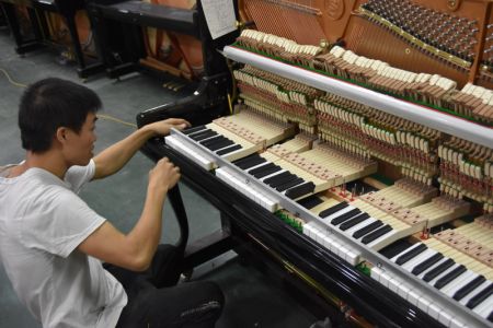 (miniature) Un travailleur ajuste un piano dans une entreprise de pianos du district de Deqing