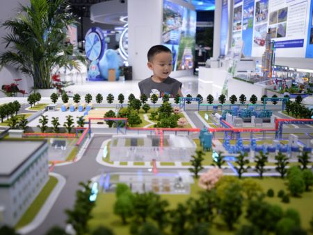 (miniature) Un enfant observe une maquette du projet intégré de production d'hydrogène hors réseau de l'énergie éolienne de Tieling de Huadian lors de la 8e Exposition Chine-Eurasie