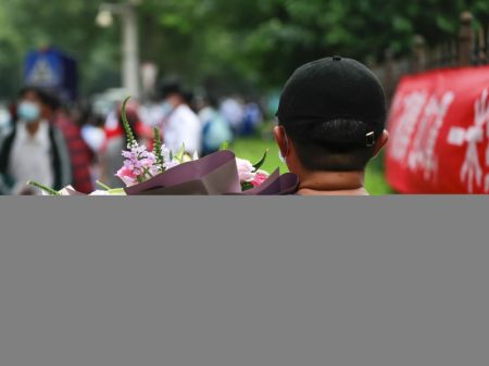 (miniature) Le père d'un candidat attend devant un site d'examen avec un bouquet de fleurs