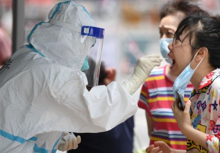 (miniature) Un membre du personnel médical en combinaison de protection prélève un échantillon de gorge sur une femme pour des tests d'acide nucléique dans le quartier de Baihedong dans l'arrondissement de Liwan à Guangzhou
