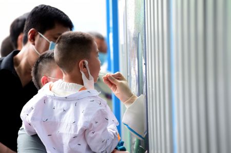 (miniature) Un membre du personnel médical prélève un échantillon de gorge sur un enfant pour des tests d'acide nucléique dans un hôpital dans le district de Feixi