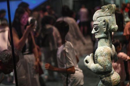 (miniature) Un visiteur prend la pose d'une statue en bronze debout pour des photos lors d'une exposition intitulée Dévoiler Sanxingdui et Jinsha de l'ancienne civilisation Shu au Musée du Grand Canal de Beijing