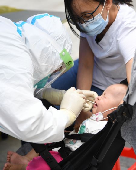(miniature) Un membre du personnel médical en combinaison de protection prélève un échantillon de gorge sur un bébé pour des tests d'acide nucléique dans le quartier de Baihedong dans l'arrondissement de Liwan à Guangzhou