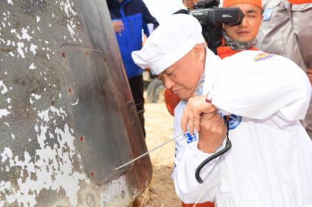 (miniature) Un membre du personnel examine la capsule de retour de la version d'essai du vaisseau spatial habité chinois de nouvelle génération sur le site d'atterrissage de Dongfeng