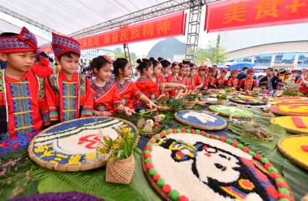 (miniature) Des &eacute;l&egrave;ves d'&eacute;cole primaire regardent les cr&eacute;ations de candidats &agrave; un concours de plats color&eacute;s &agrave; base de riz gluant sur une place culturelle du district autonome Yao de Dahua