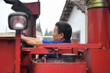 (miniature) Un agriculteur répare une moissonneuse dans un champ du village de Tongxing à Yiyang